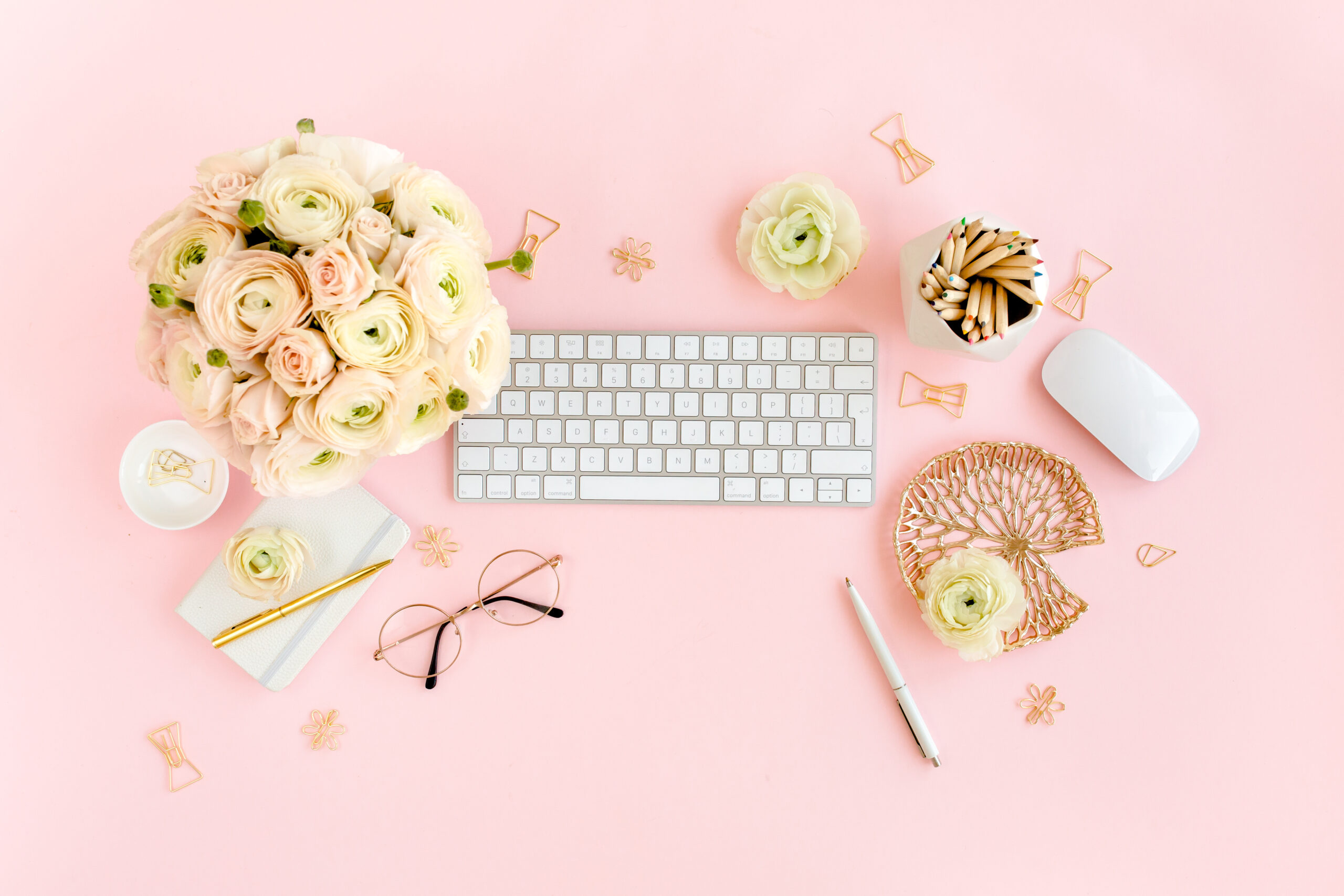 Stylized, pink women’s home office desk. Workspace with computer, bouquet ranunculus and roses, clipboard, feminine golden fashion accessories isolated on pink background. Flat lay. Top view.